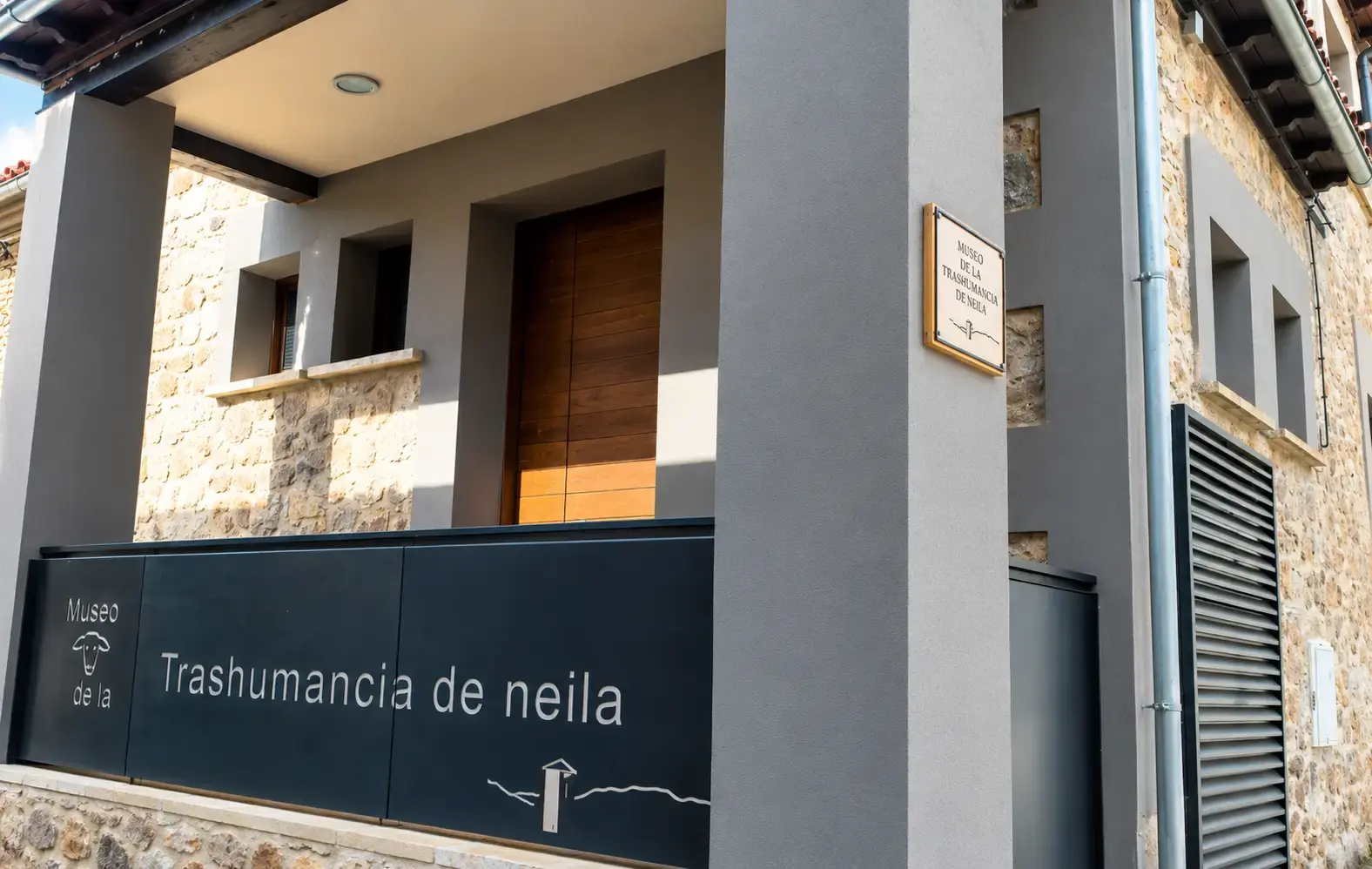 Fachada y entrada del Museo de la Trashumancia de Neila, con cartel identificativo y revestimiento de piedra y madera.