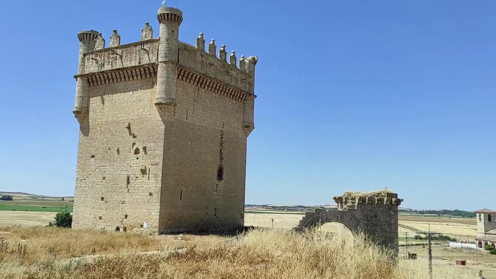Imponente torre del homenaje del Castillo de Belmonte de Campos con garitones y arco de piedra en ruinas en primer plano.