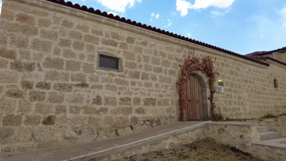 Detalle de la fachada de piedra de sillería de la Ermita de Santa Eulalia en Avellanosa del Páramo, mostrando una pequeña ventana rectangular y una puerta de madera con decoración vegetal. Detalle de la fachada de piedra de sillería de la Ermita de Santa Eulalia en Avellanosa del Páramo, mostrando una pequeña ventana rectangular y una puerta de madera con decoración vegetal.