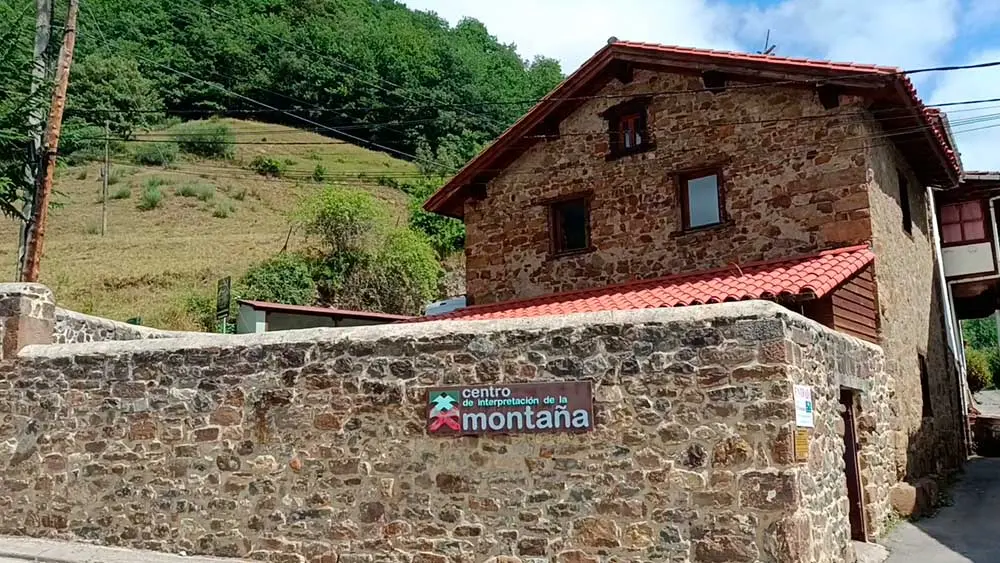 Edificio de piedra tradicional de dos plantas con tejado de teja roja y un muro delantero que muestra un cartel del Centro de Interpretación de la Montaña.