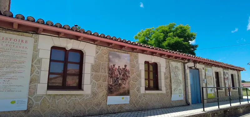 Fachada exterior de un edificio de piedra decorado con paneles informativos y carteles históricos en Burgos, bajo un cielo azul.
