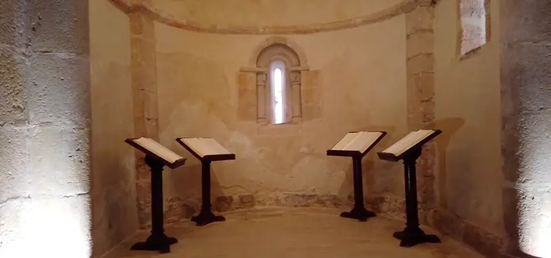 Interior del ábside de piedra de estilo románico en el Centro del Románico de las Merindades en Medina de Pomar, Burgos, con atriles y libros expuestos.