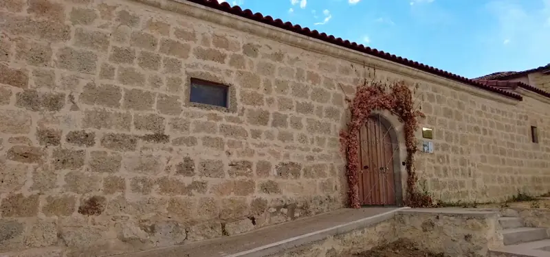 Fachada exterior de piedra del Museo Etnográfico de la Merindad de Sotoscueva en Burgos, con una puerta de madera en arco y vegetación decorativa.