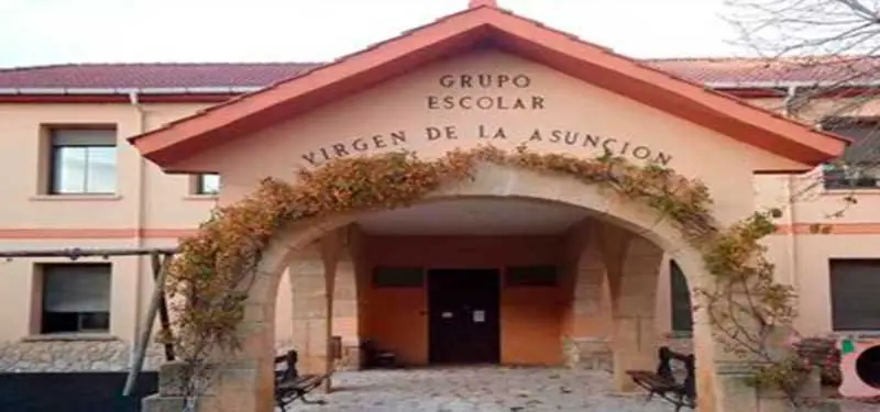 Fachada del edificio de la escuela en Robledo, destacando un porche arqueado con vegetación trepadora en la entrada principal.