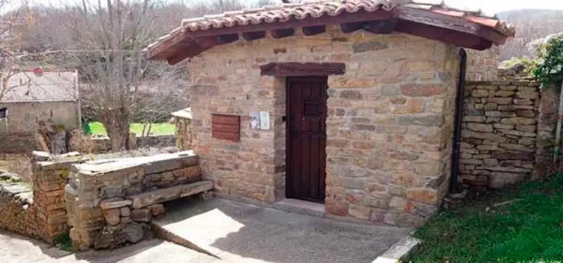 Comparativa visual deslizante de una pequeña construcción rústica de piedra con puerta de madera y tejado de tejas en una zona rural.
