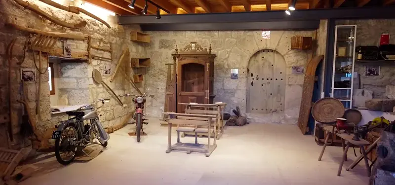 Interior del Museo Etnográfico del Concejo de Lodoso en Burgos, con una sala amplia de paredes de piedra que expone herramientas agrícolas antiguas, motocicletas y mobiliario tradicional.