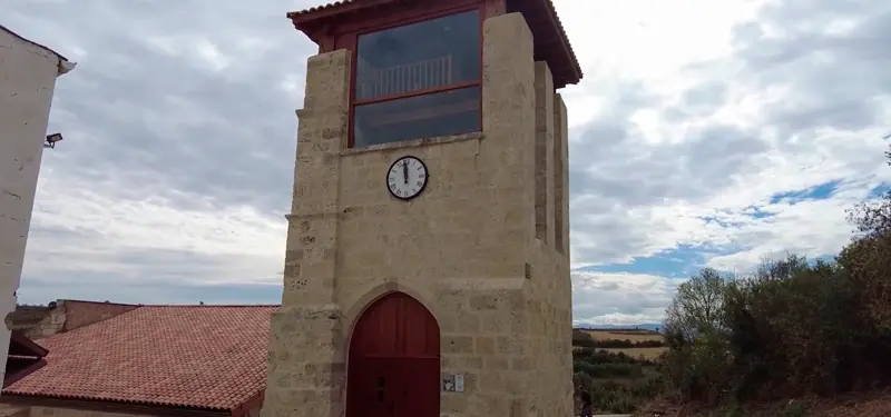 Torre de piedra con reloj y grandes ventanales de madera en Burgos, bajo un cielo nublado.