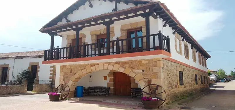 Fachada exterior de un edificio moderno revestido en piedra rústica y grandes ventanales de cristal con marcos oscuros, incluyendo una puerta de entrada lateral.
