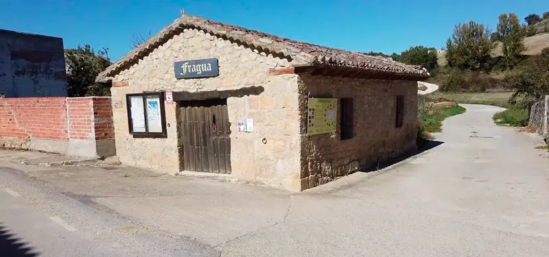 Vista exterior del edificio de piedra del Museo de la Fragua en Lodoso, Burgos, situado junto a un camino rural y una carretera asfaltada.
