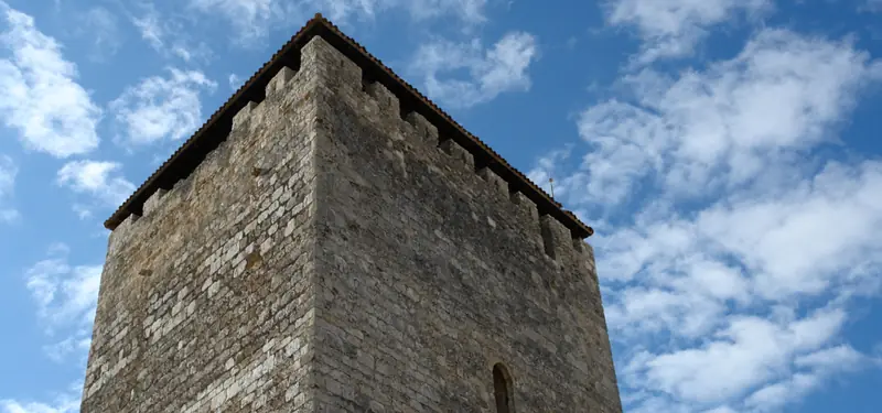 Fotografía en contrapicado de la torre de piedra del Torreón de Haza en Burgos contra un cielo azul con nubes.