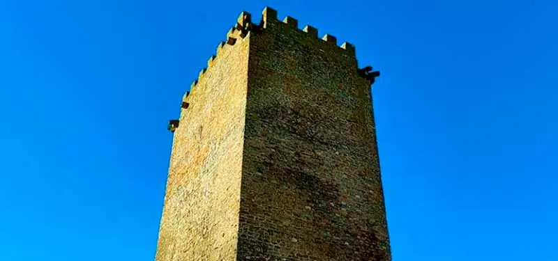 Torre defensiva medieval de piedra con almenas en la parte superior contra un cielo azul intenso.