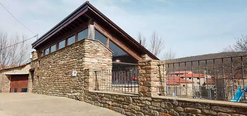 Casa rural de piedra con grandes ventanales y tejado de madera en un pueblo de montaña